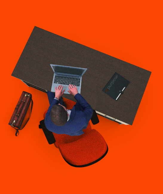 A man sitting at a desk on his computer with a Purpose logo folder.